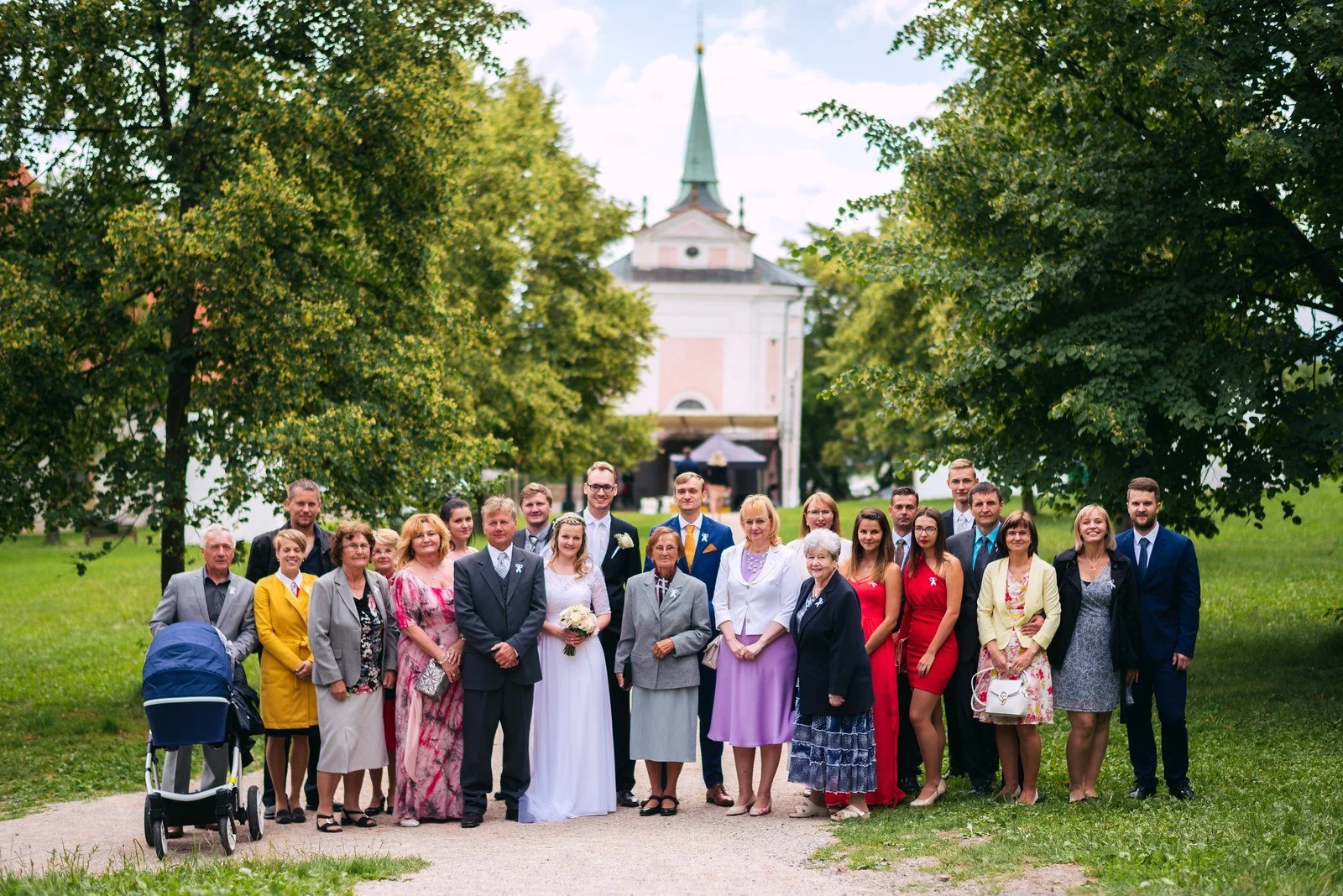 Velká skupina dospělých a dětí pózuje před světlým průčelím kostela.