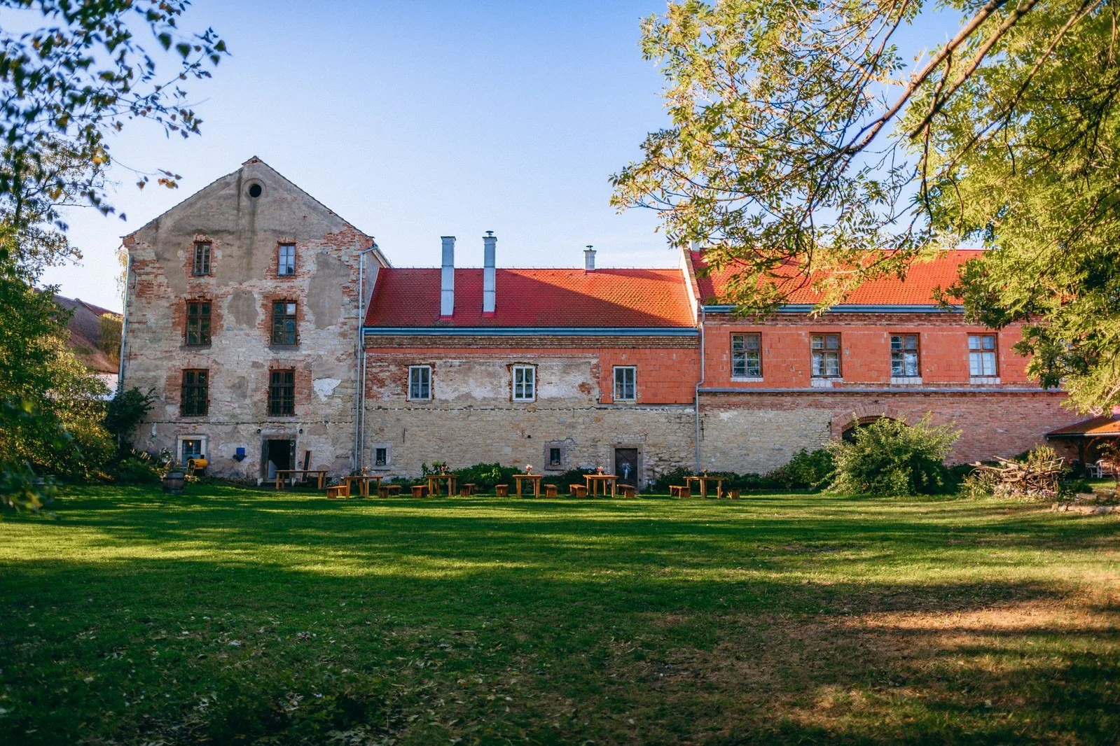 Široký pohled na historickou budovu a zelenou zahradu uvádí místo děje.