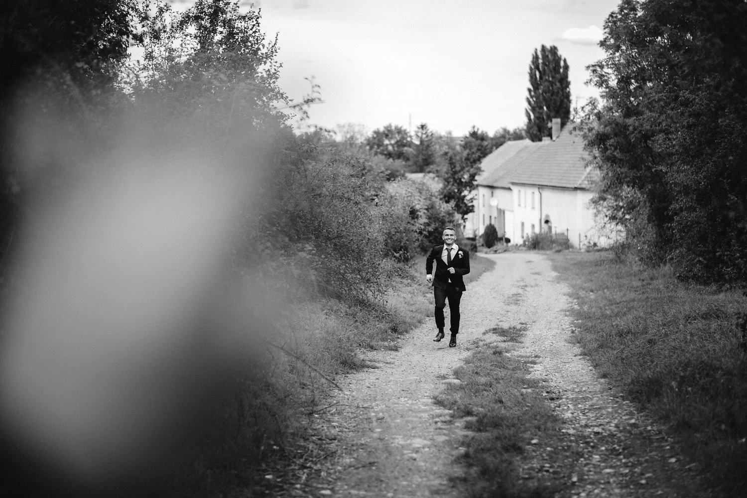 Černobílý vzdálený pohled na pár kráčející po venkovské cestě k domu.