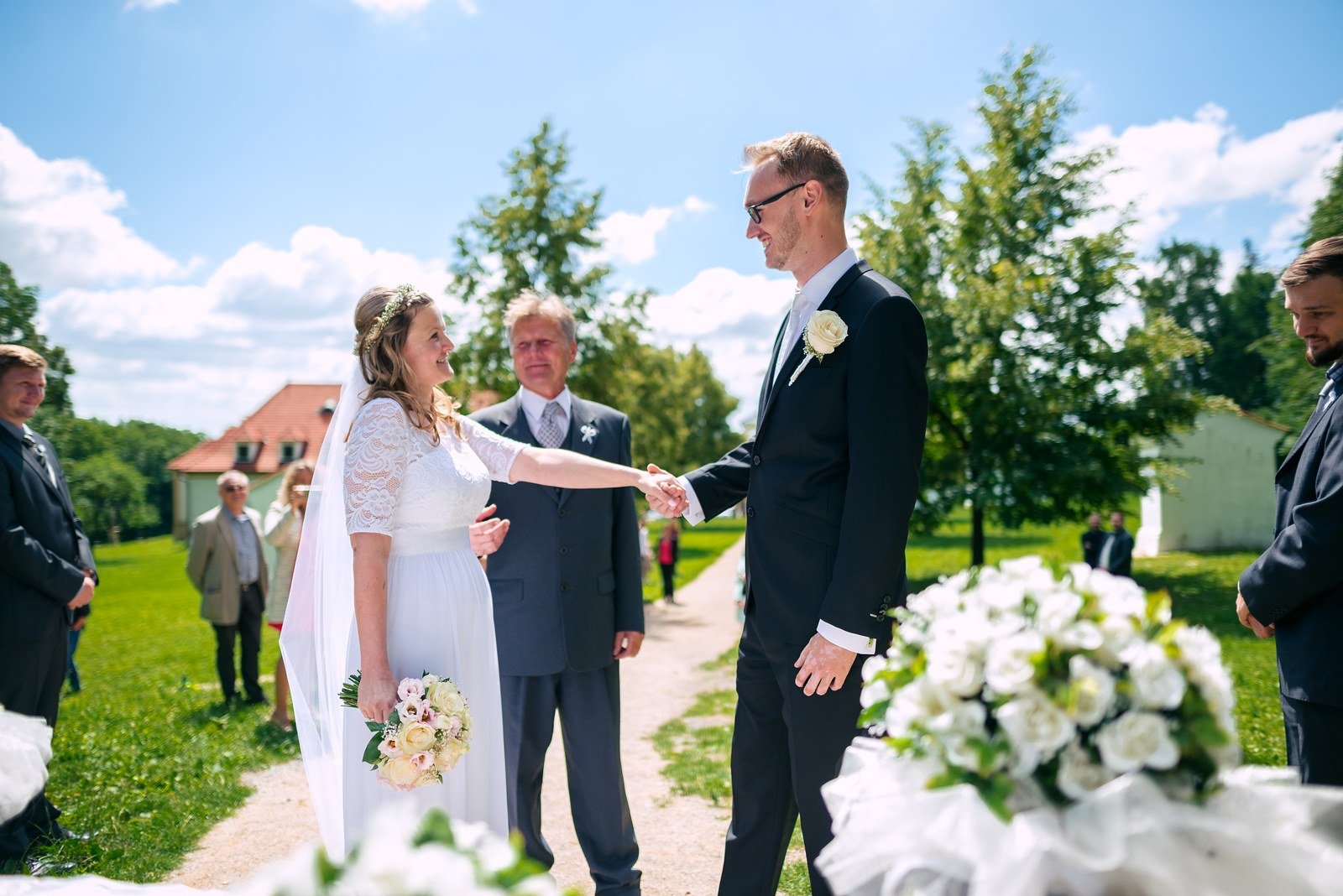 Dva muži se připravují v pokoji, jeden v bílé košili stojí zády k fotoaparátu.
