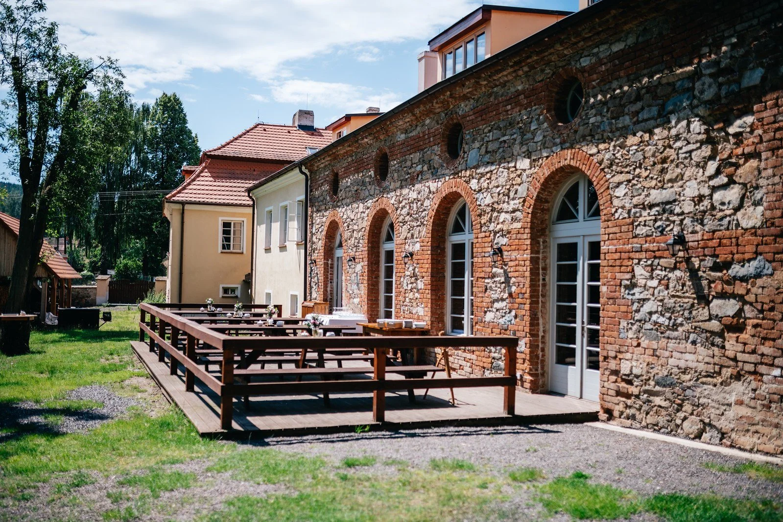 Cihlová budova se zahradní terasou a dřevěnými stoly.
