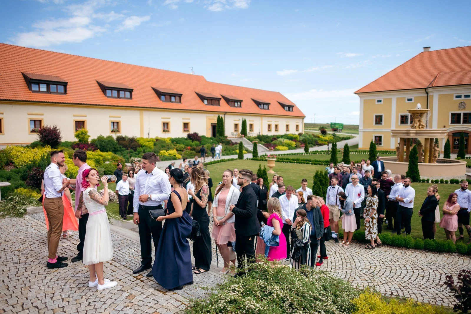 Klára a Lukáš se líbají pod slavobránou před svatebními hosty.