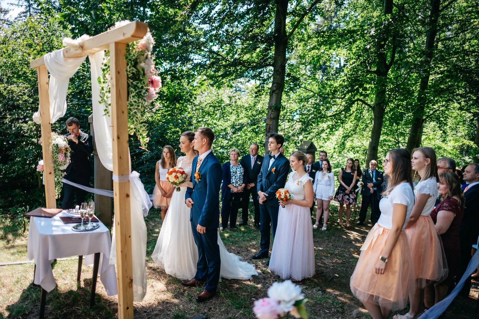 Široký pohled zachycuje obřad pod bílými závěsy v lese.