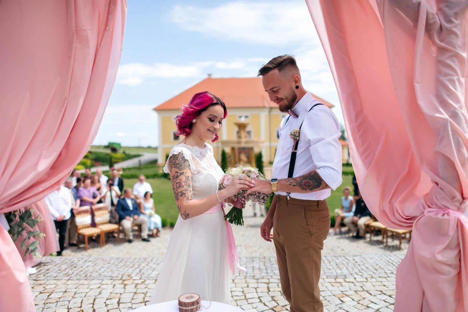 Malá družička v bílých šatech kráčí trávou uličkou mezi hosty.