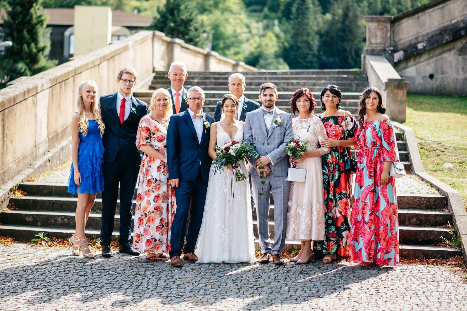 Barevná skupina hostů stojí na širokých schodech.