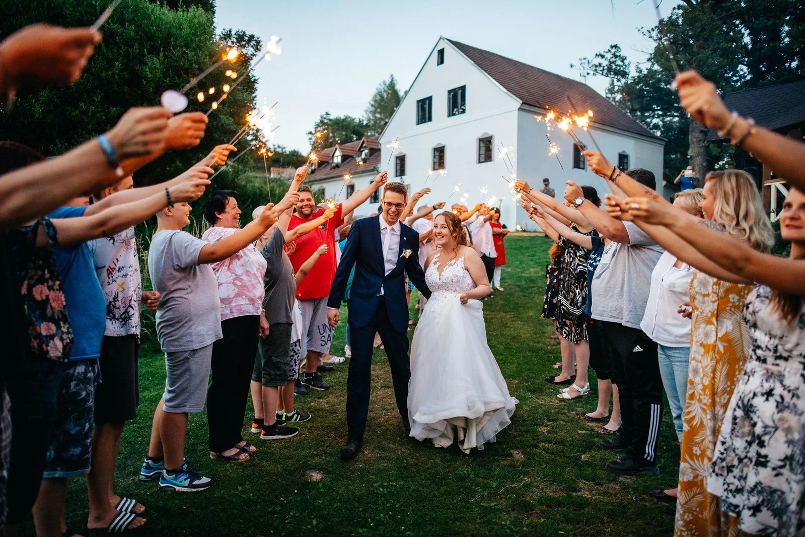 Hosté drží zapálené prskavky nad párem procházejícím večerní uličkou.