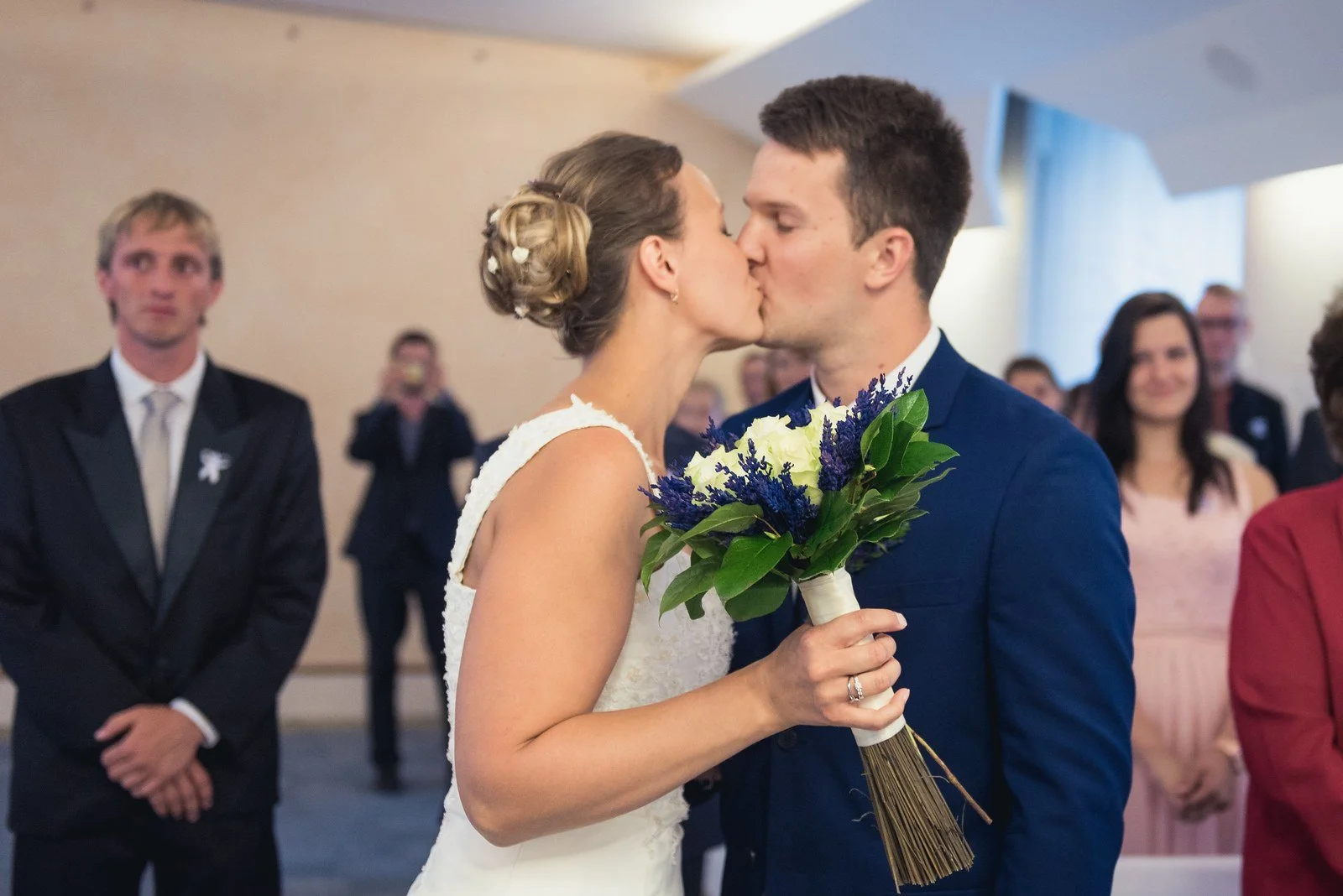 Novomanželé se líbají s kyticemi v rukou před hosty.
