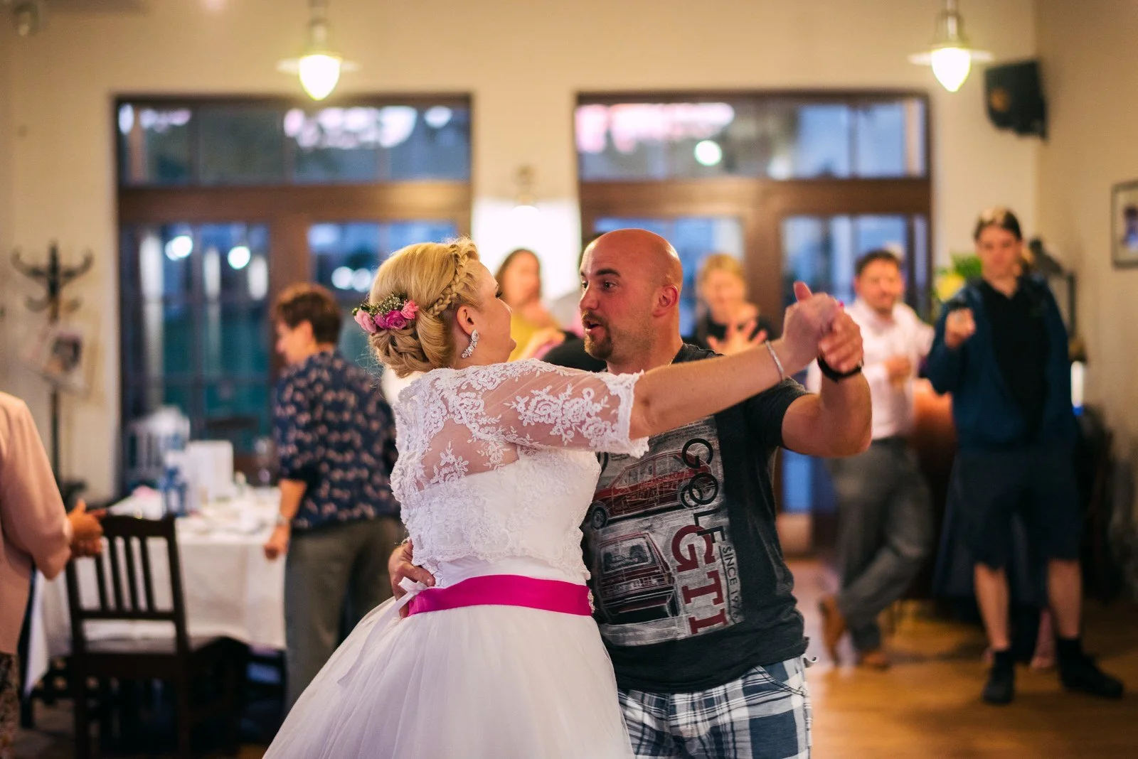 Žena v bílých šatech tančí s rozpaženou ženou v pruhovaném oblečení.