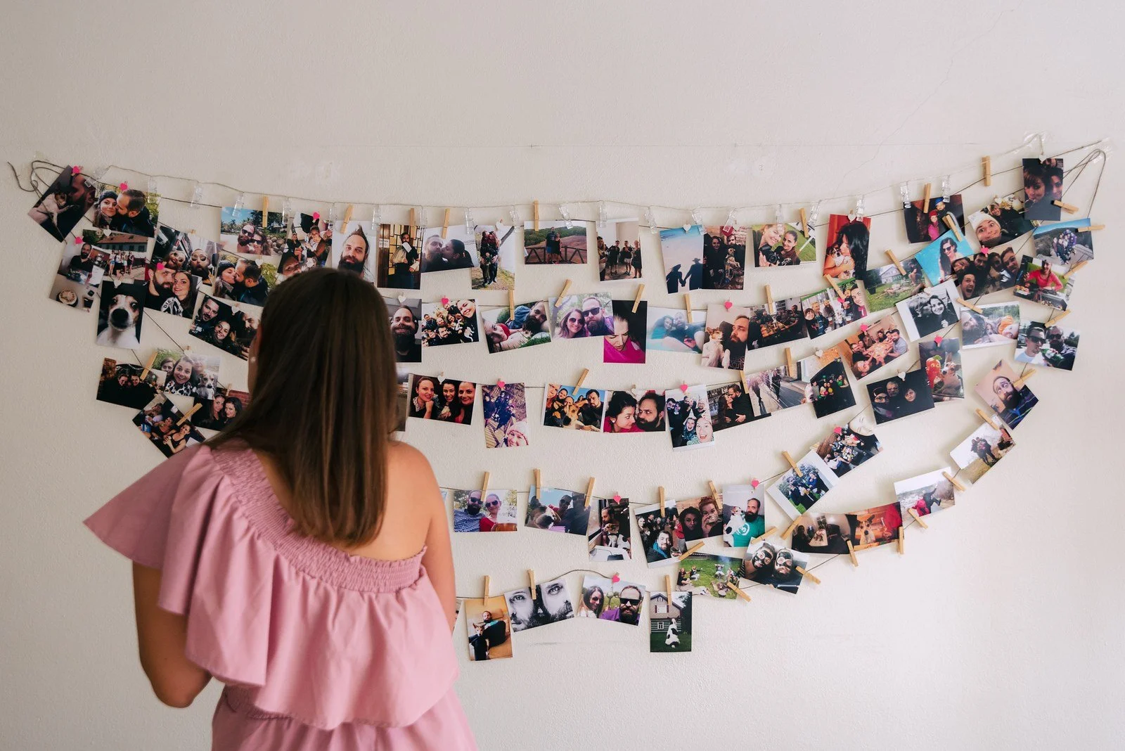 Dívka v růžových šatech stojí před velkým srdcem složeným z mnoha fotografií.