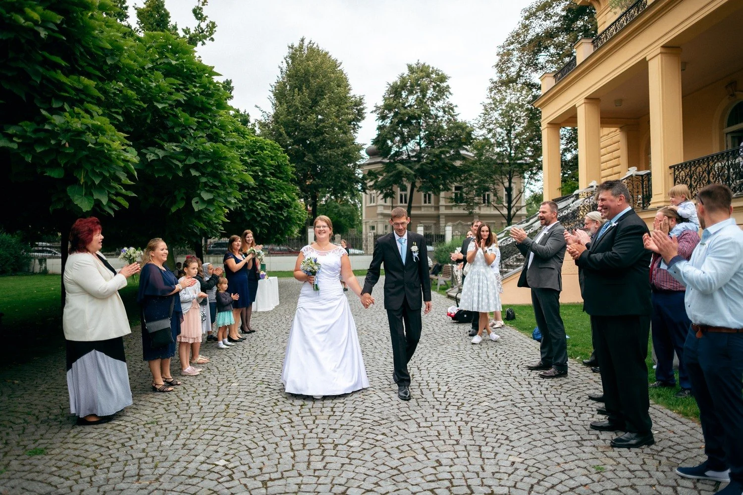 Novomanželé procházejí uličkou vytvořenou hosty na nádvoří.