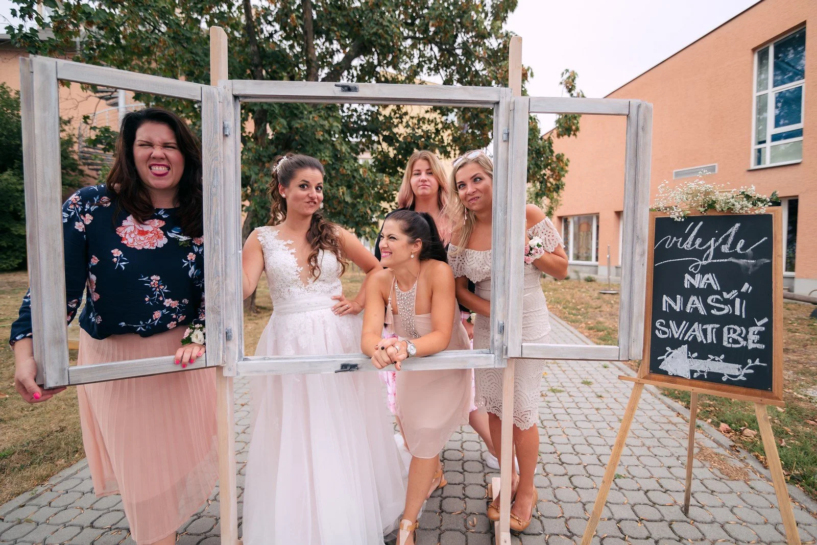 Několik lidí pózuje venku v ozdobném rámu drženém před fotoaparátem.