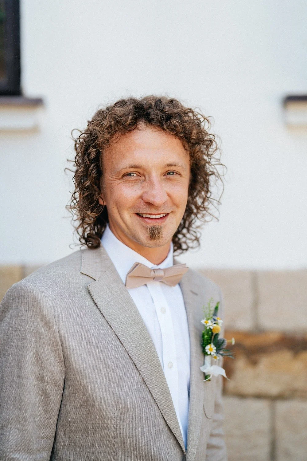Portrét Norberta ve světlém obleku a motýlku před kamennou zdí
