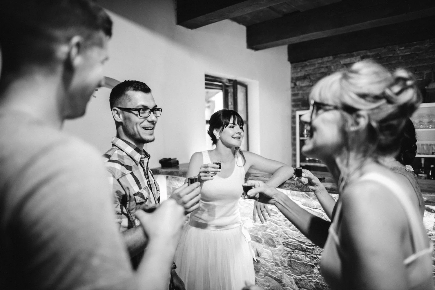 Černobílá fotografie zachycuje Radku se skleničkou při rozhovoru mezi hosty.