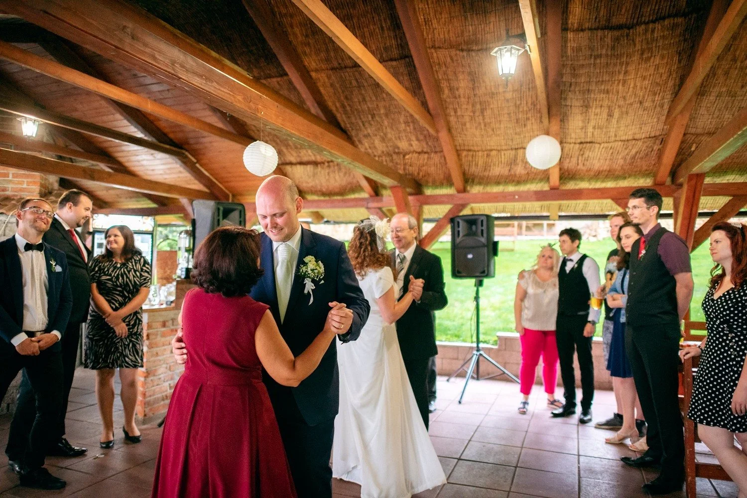 Ženich tančí se ženou v červených šatech před hosty.