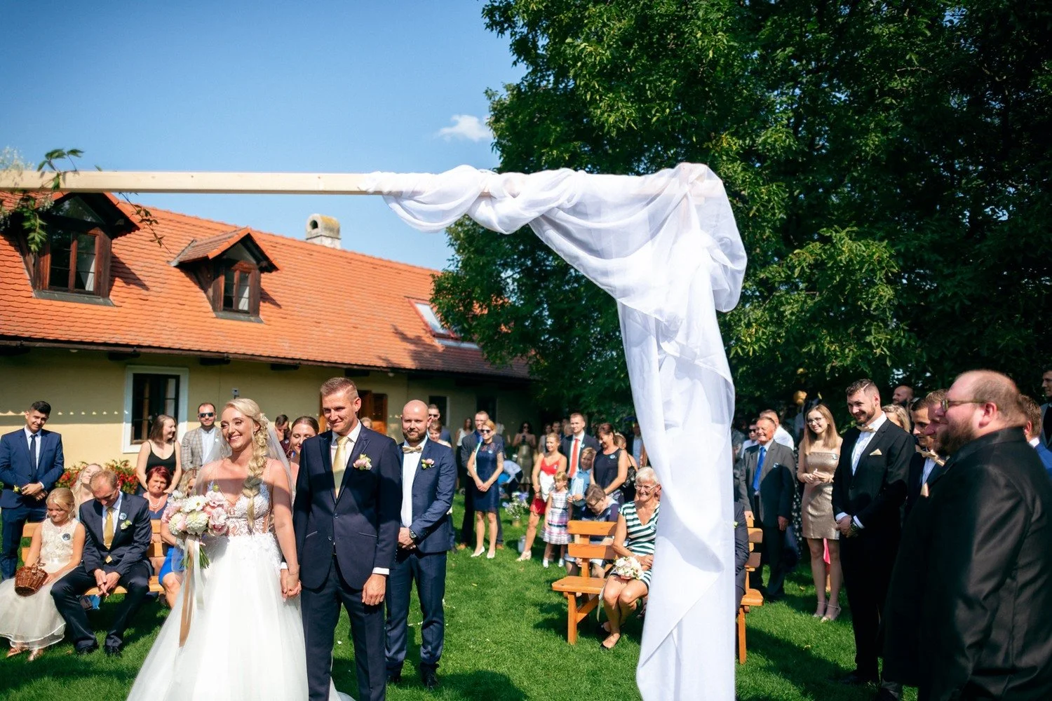 Větrem nadzvednutá látka nad párem u obřadního oblouku