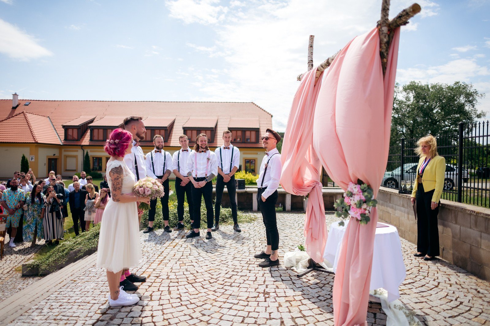 Lukáš čeká v tmavém obleku pod slavobránou ozdobenou bílou látkou.