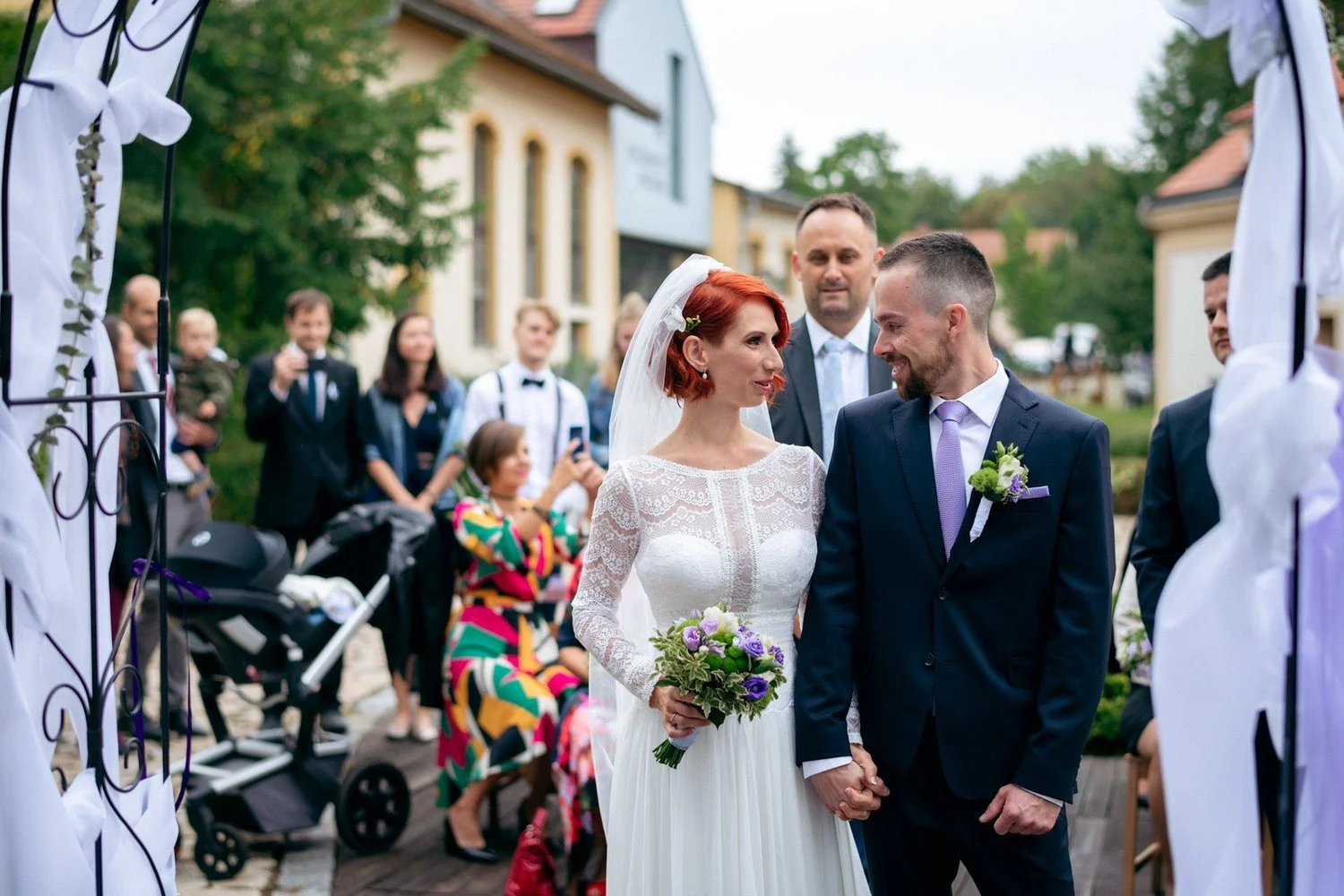 Martina stojí u obřadního oblouku po boku staršího muže.