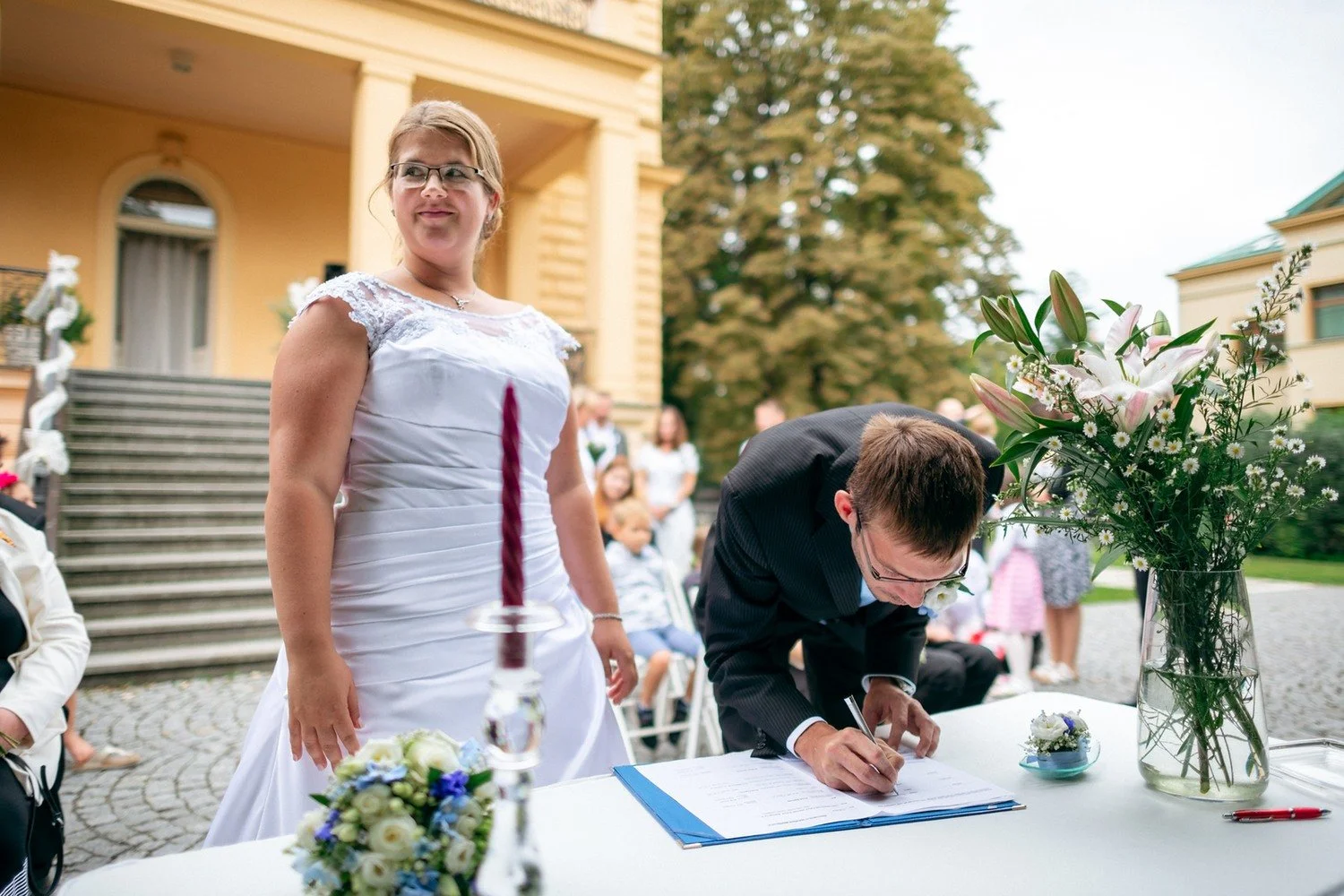Ženich se sklání nad stolem a podepisuje dokument.