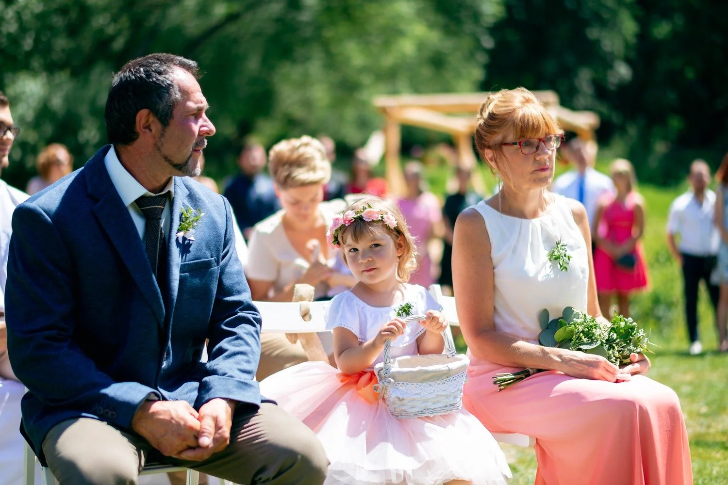 Muž v modrém saku, žena v růžové sukni a malá dívka pozorně sledují obřad.