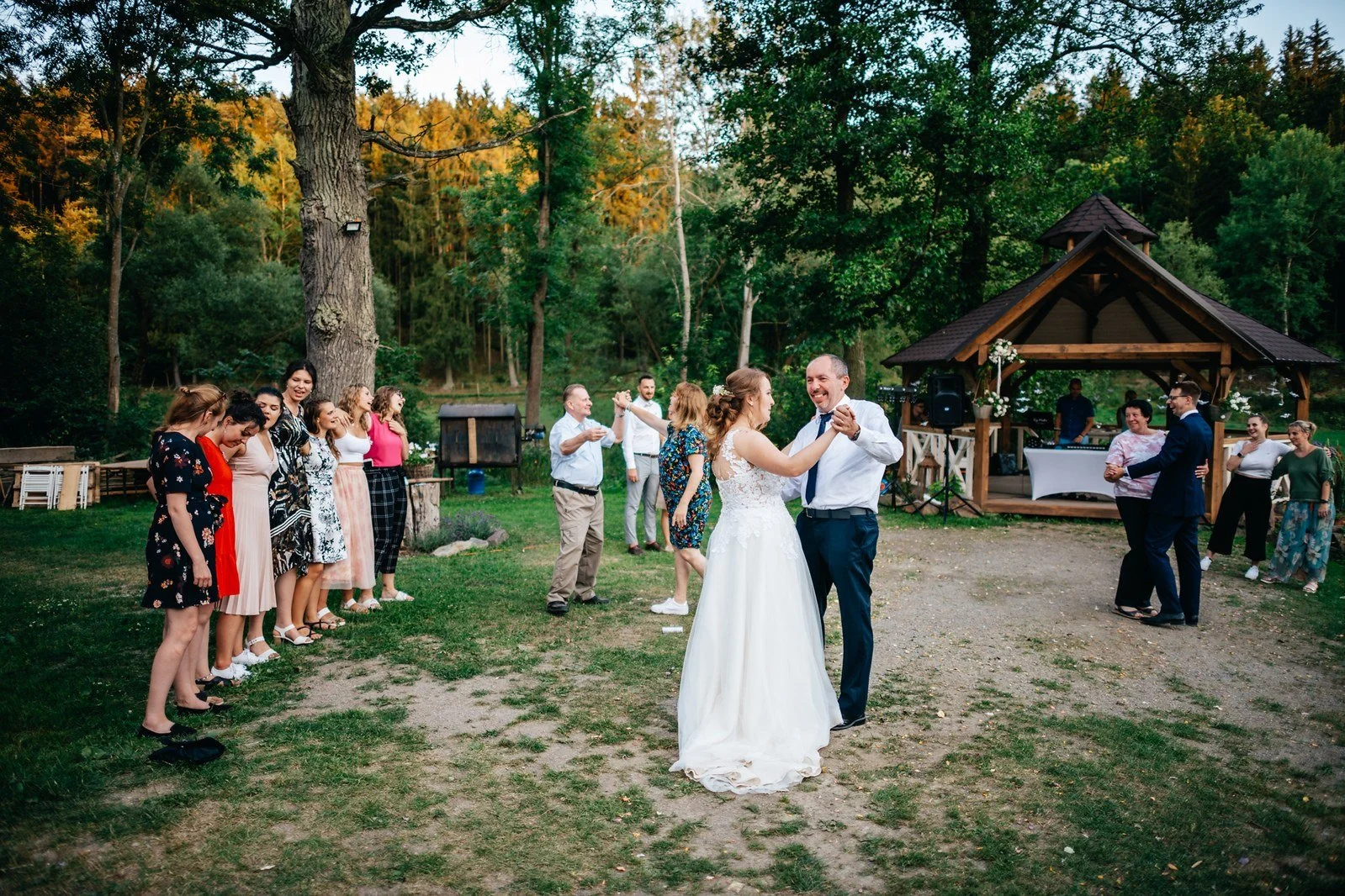 Nevěsta a ženich tančí venku uprostřed kruhu přihlížejících hostů.