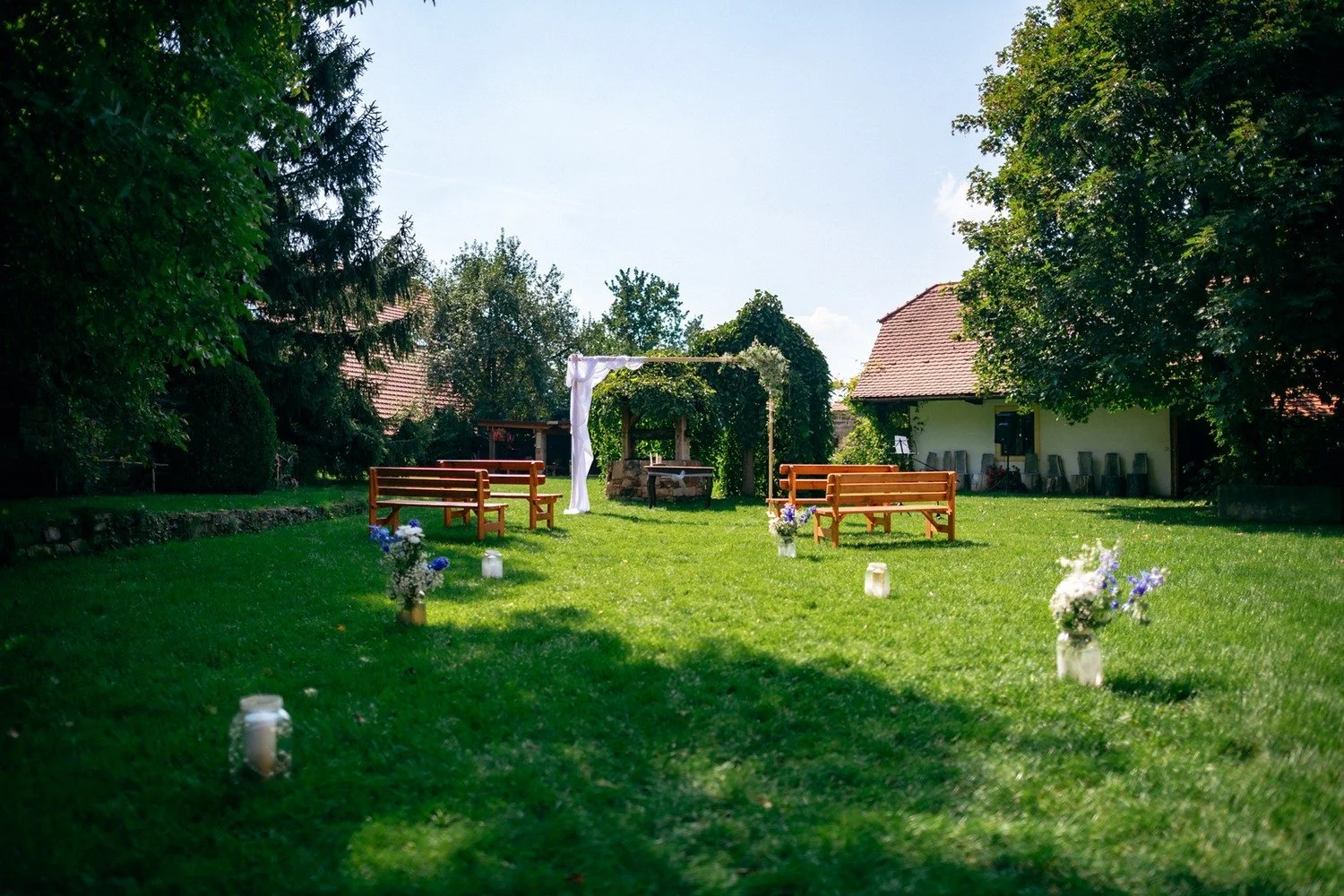 Prázdné dřevěné lavice a zelený obřadní oblouk v zahradě