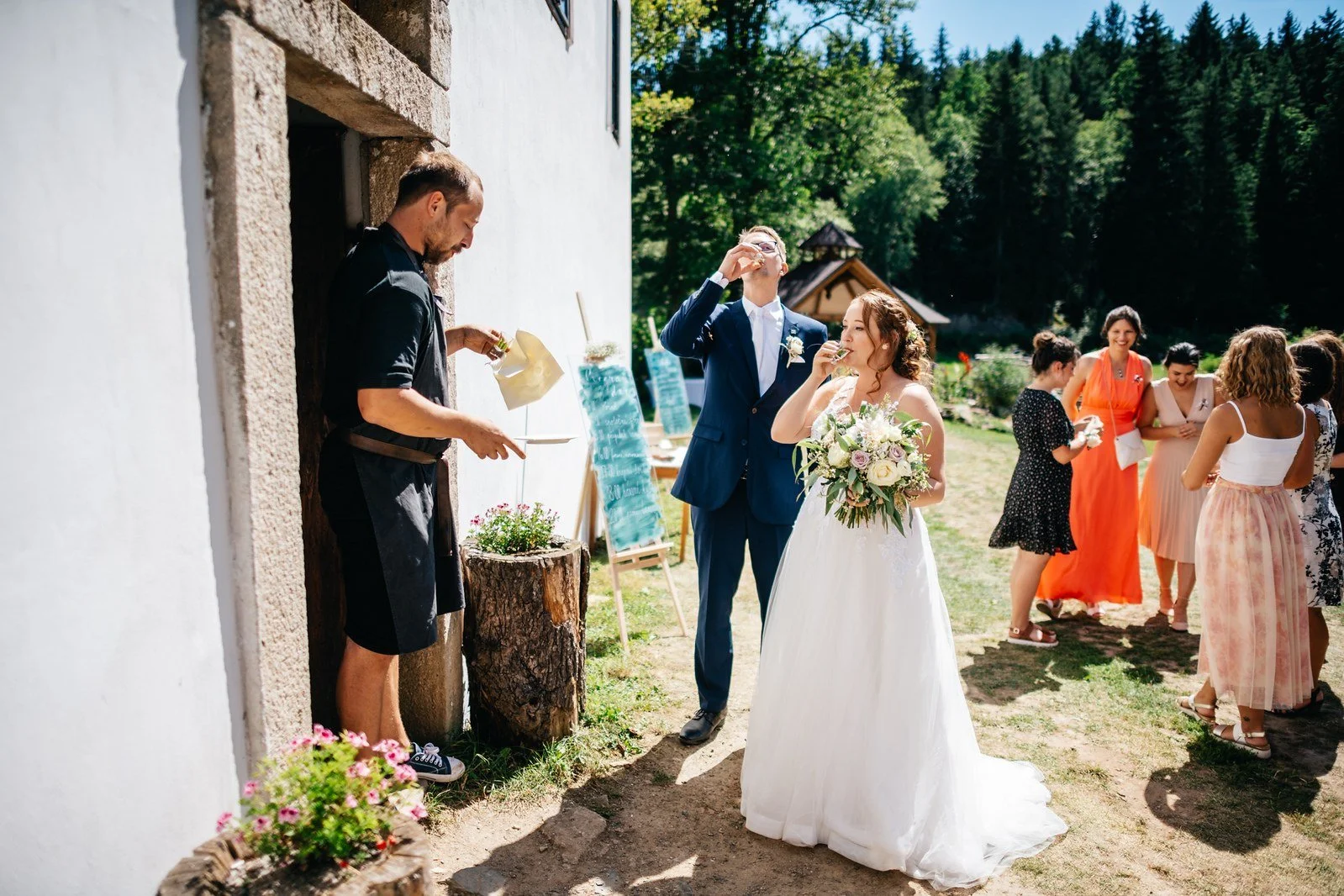 Novomanželé procházejí uličkou pod pažemi hostů zvednutými do oblouku.