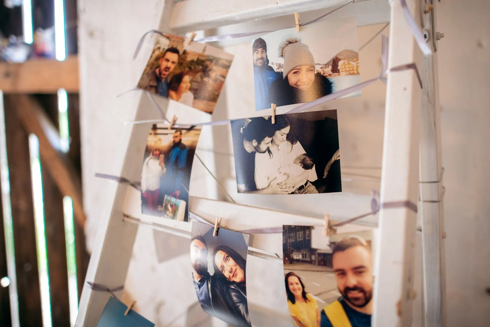 Na bílé mřížce visí kolíčky několik barevných fotografií lidí.