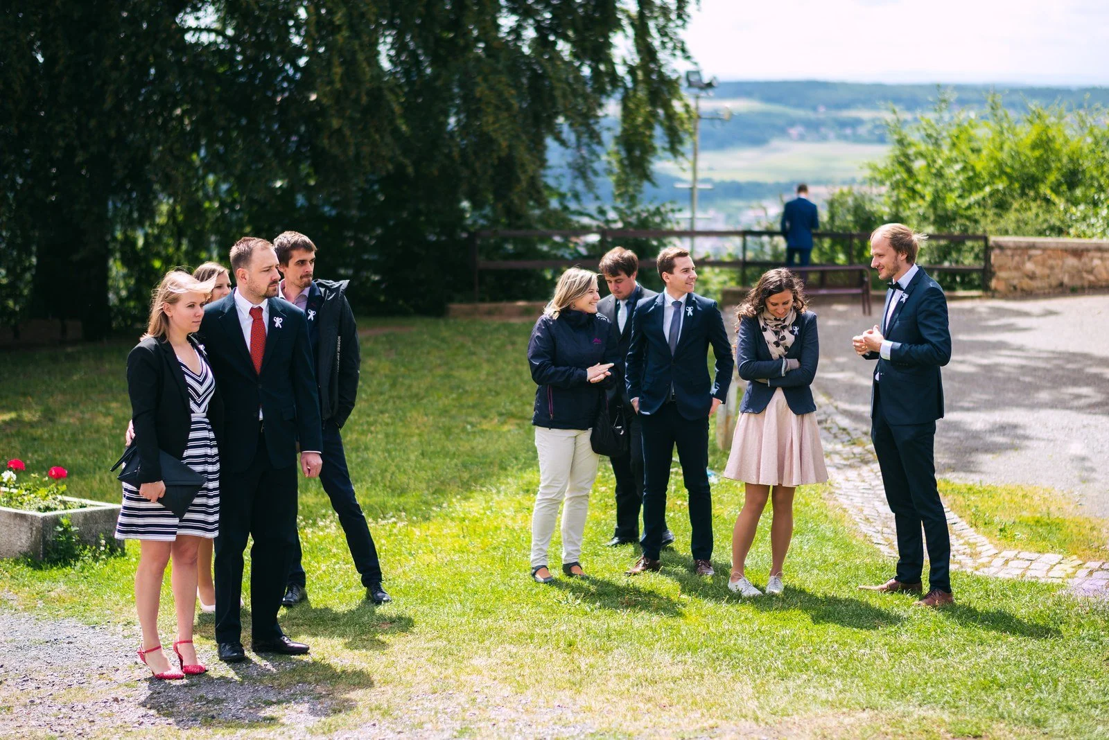Bílé svatební šaty visí na ramínku před kamennou zdí a dřevěnými dveřmi.