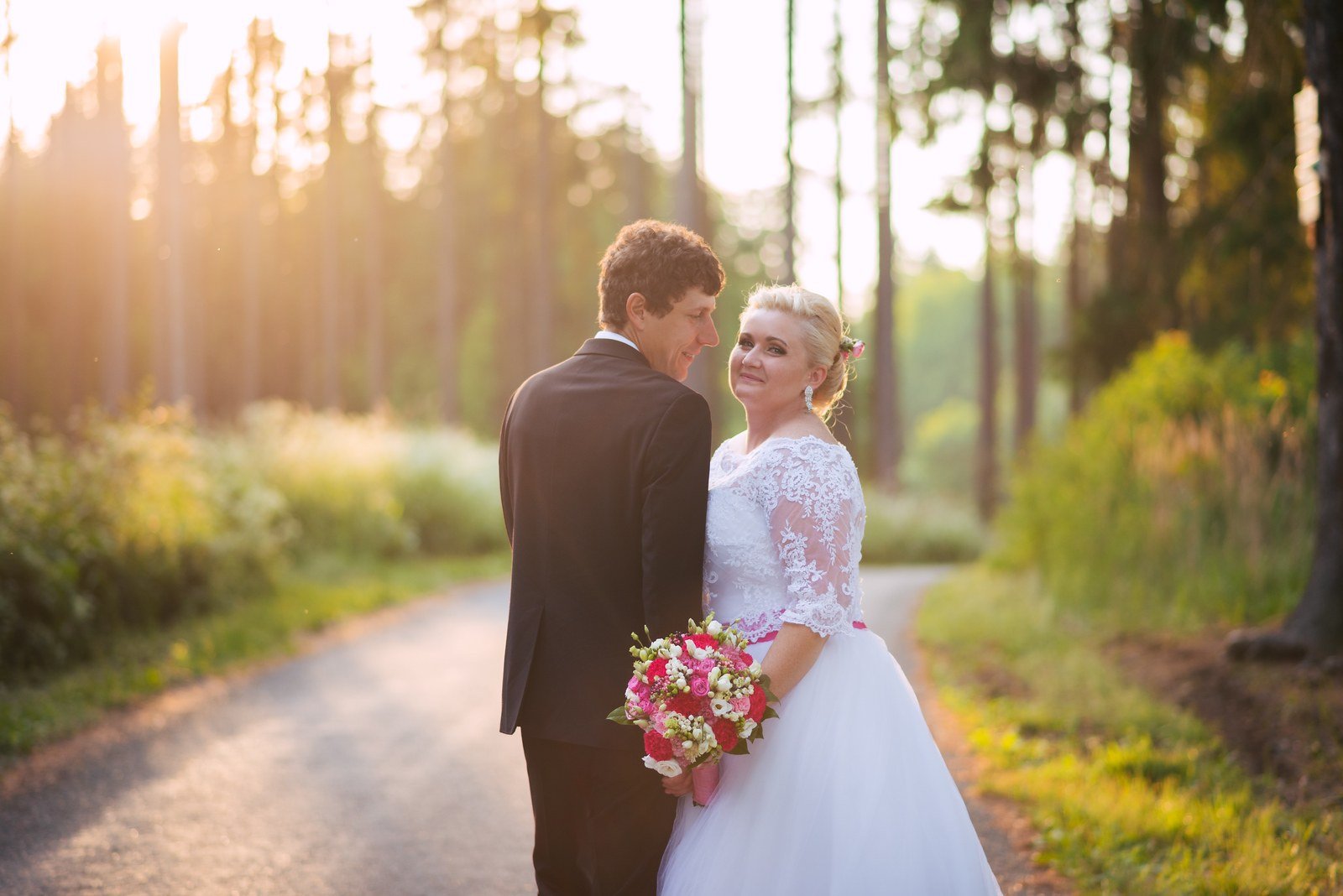 Dvojice stojí s kyticí na lesní cestě zalité zlatým protisvětlem.