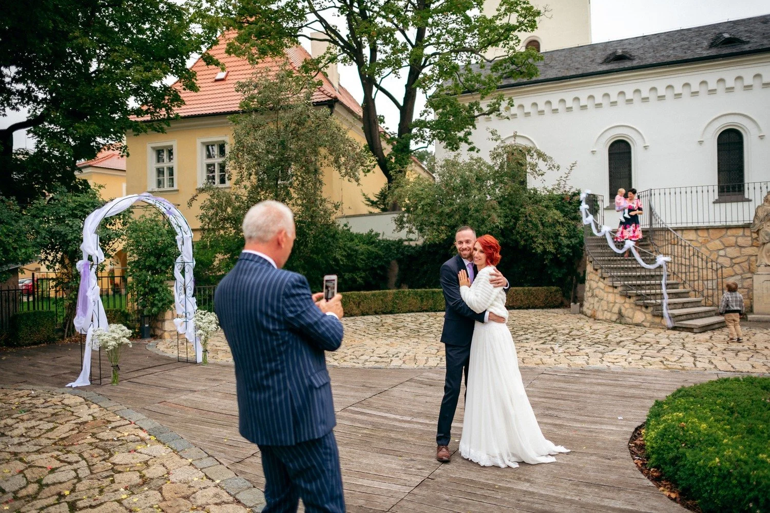 Starší muž fotografuje Martinu a Lukáše na nádvoří.