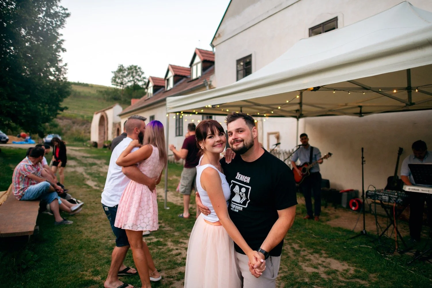 Usměvavá taneční dvojice se drží za ruce před stanem s hudebníky.