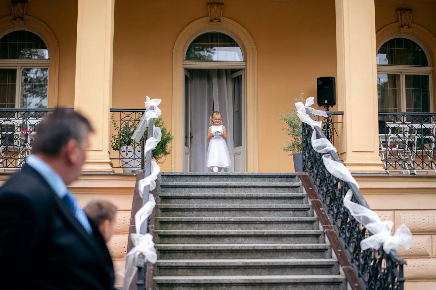 Nevěsta stojí nahoře na schodišti připraveném pro venkovní obřad.