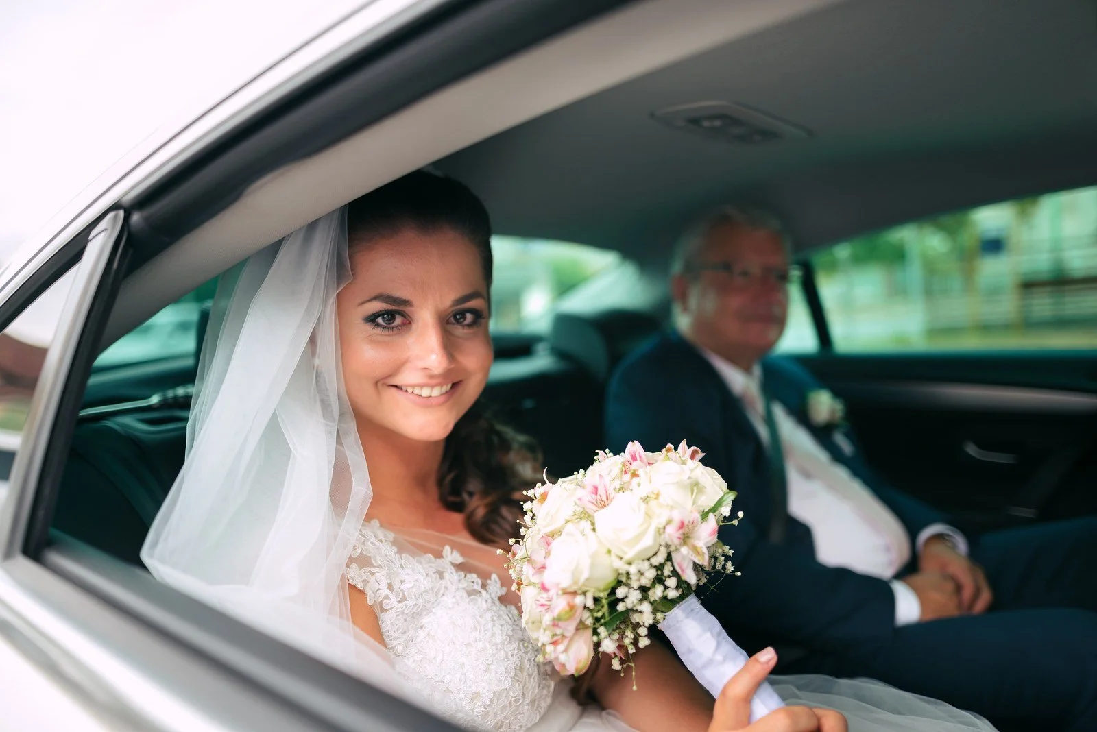 Žena s kyticí sedí u otevřeného okna automobilu a dívá se ven.