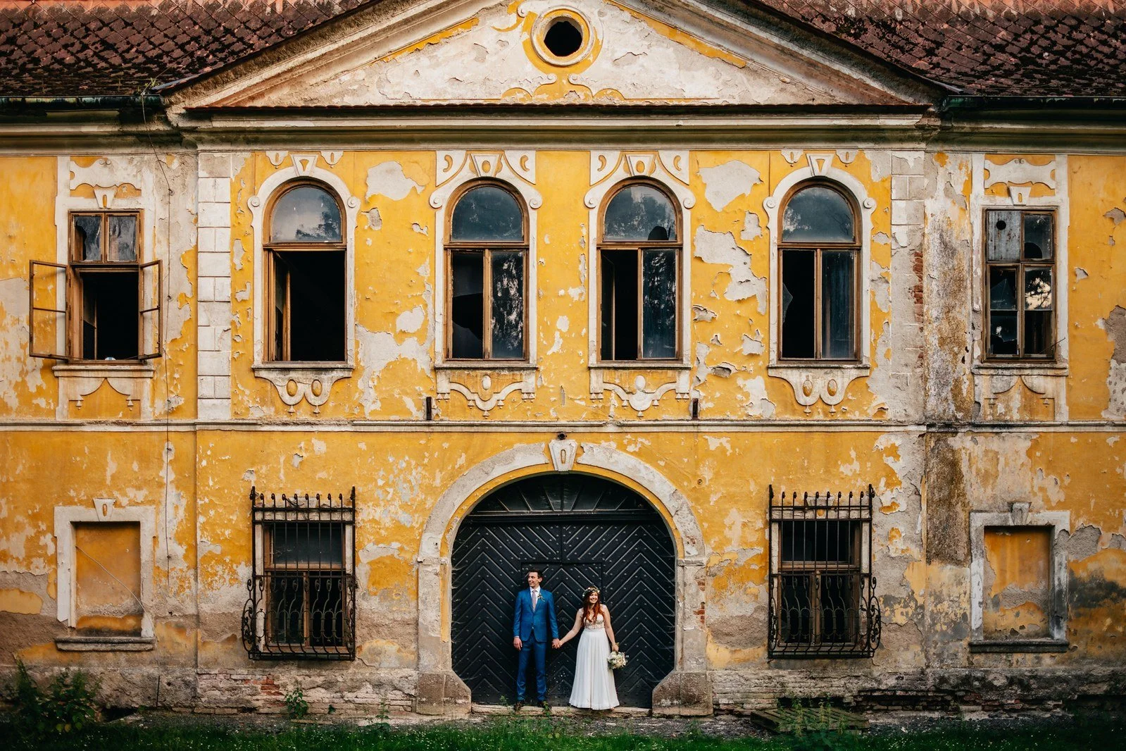 Průčelí staré žluté budovy s dvojicí ve vstupním oblouku.