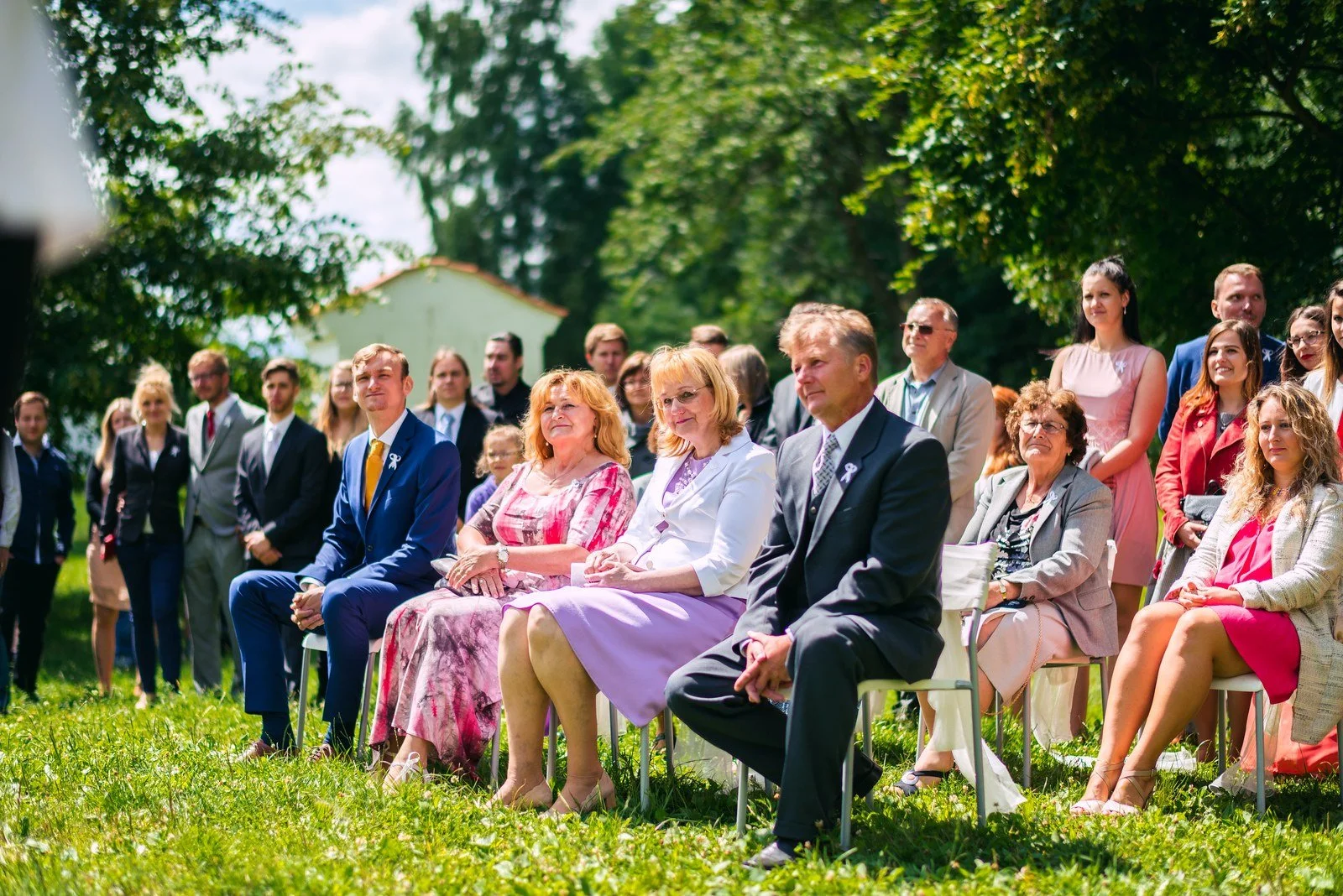 Žena připíná muži v šedé vestě bílou květinu na klopu.