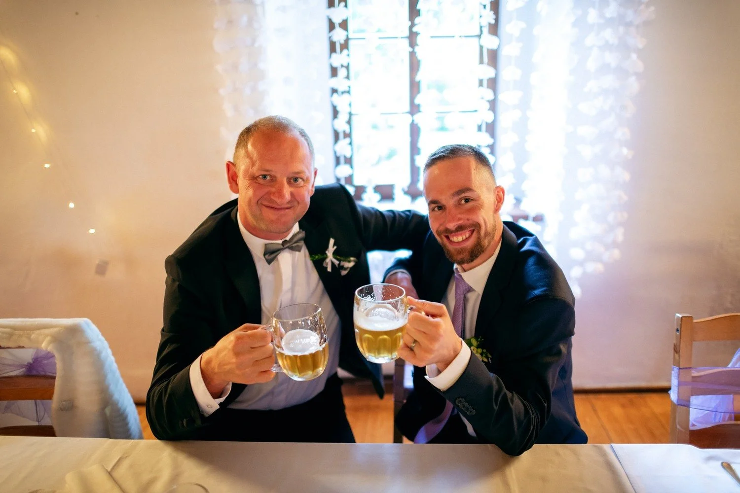 Dva muži sedící u stolu si připíjejí pivem.
