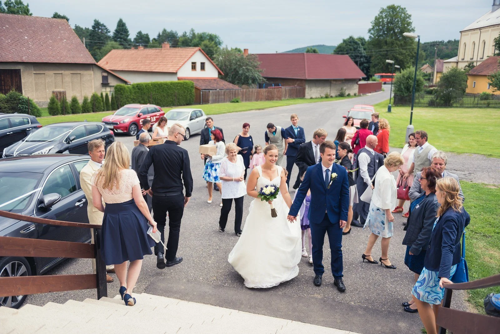 Pár prochází mezi svatebčany při příjezdu na hostinu.
