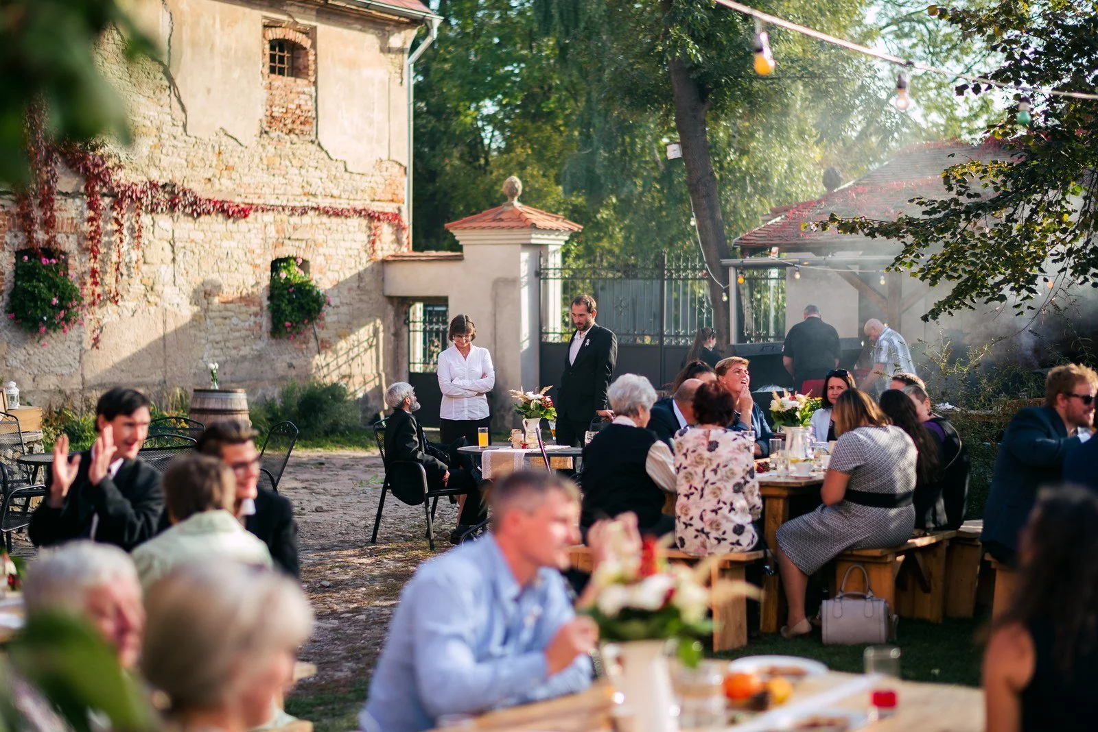 Hosté sedí u venkovních stolů na dlážděném nádvoří mezi historickými budovami.