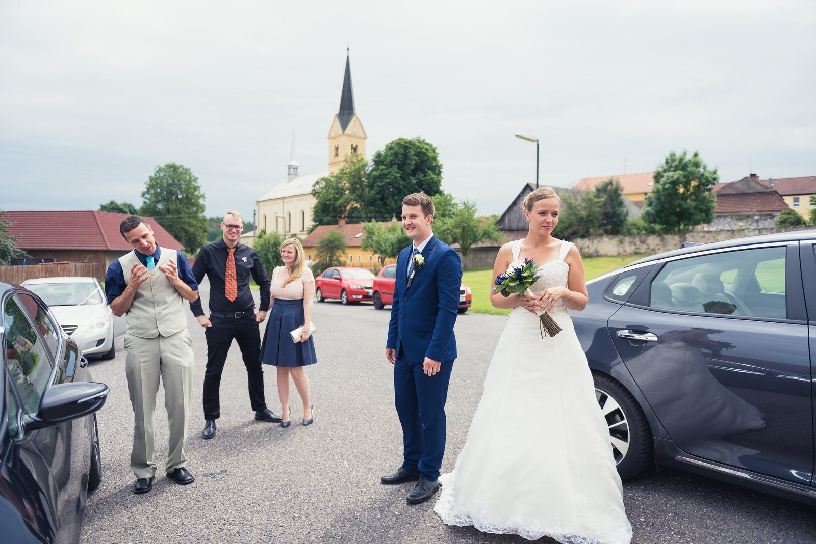 Novomanželé přicházejí od auta k čekajícím hostům.