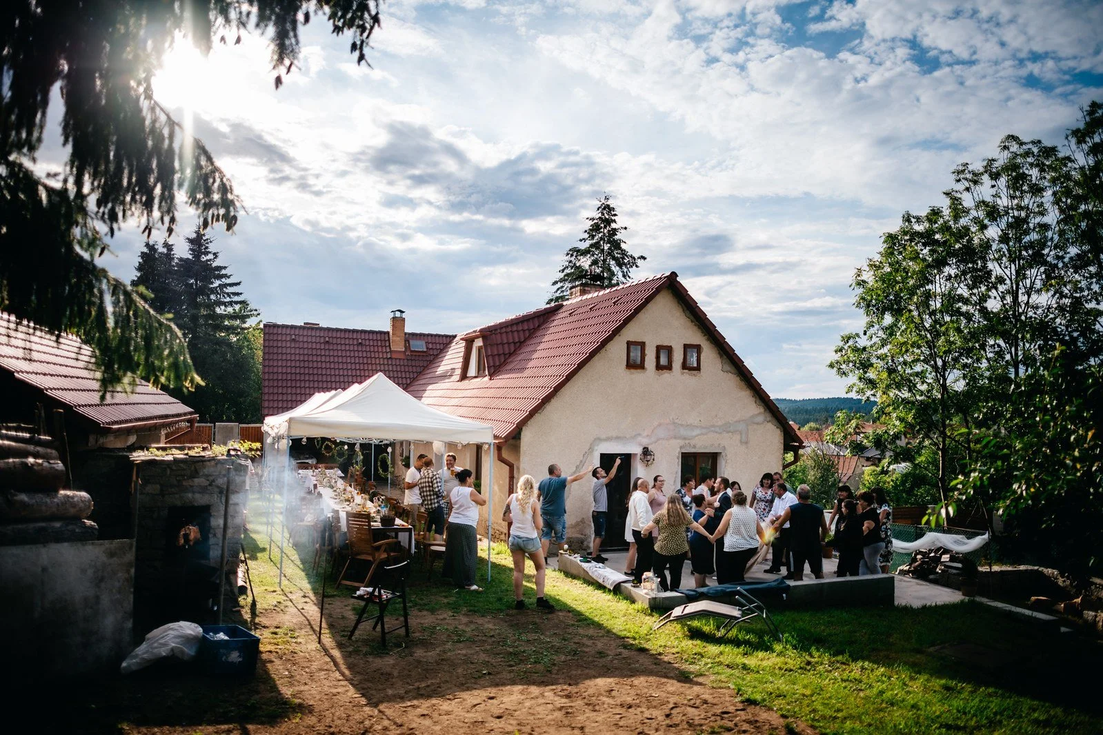 Široký pohled přes dvůr k tanečnímu dění střídá blízké emoce s prostředím a večerním světlem.