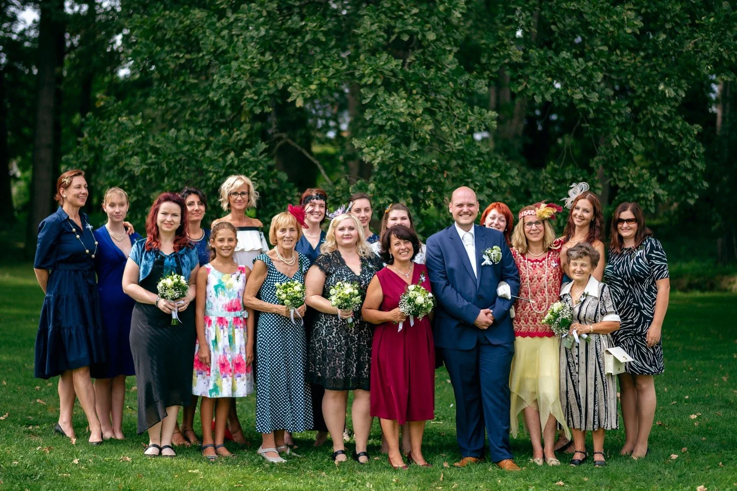 Skupina žen pózuje s párem na zámeckém trávníku.