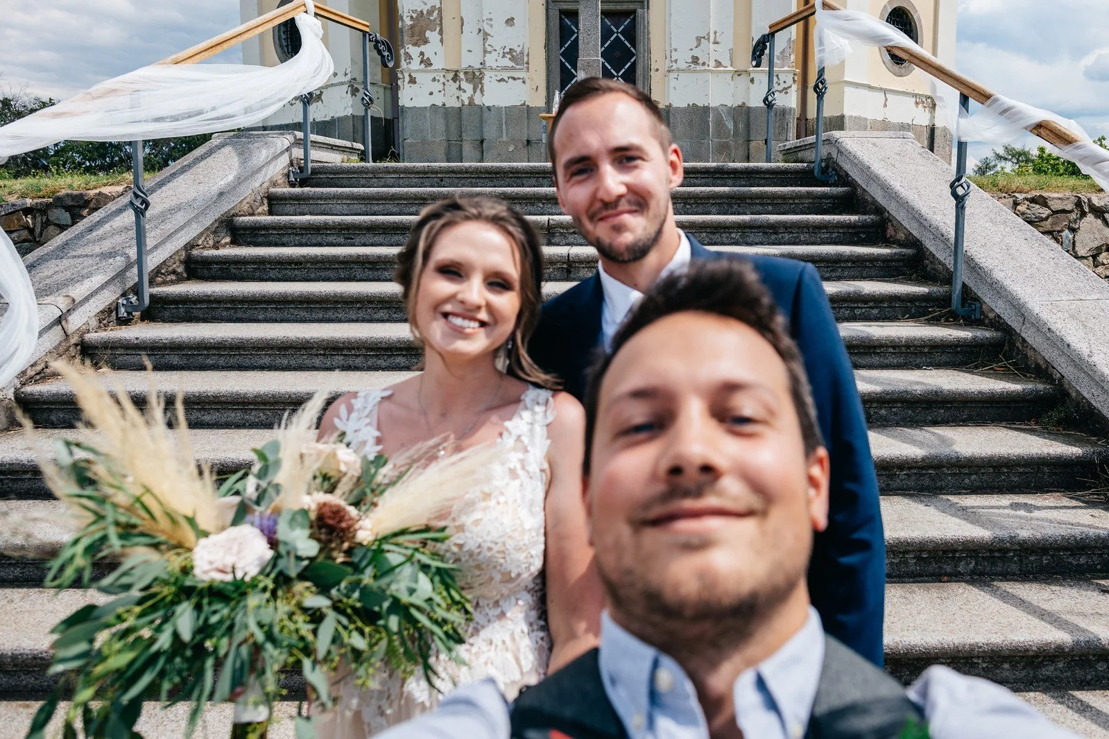 Hrátkový selfie záběr trojice na schodišti narušuje formální rytmus.