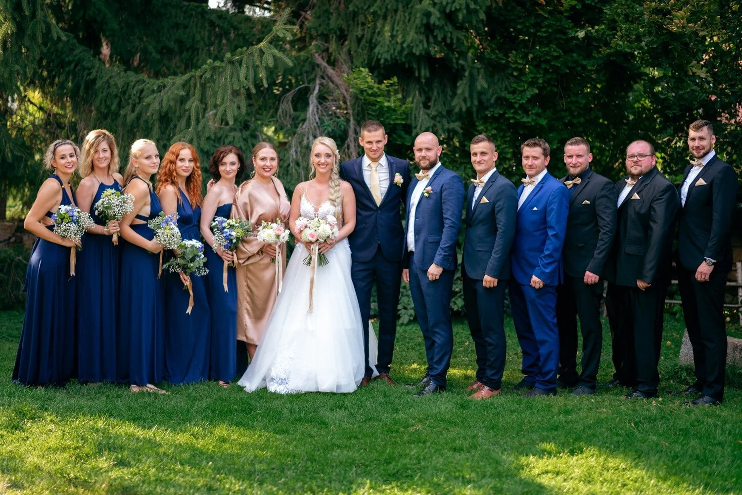 Společná fotografie páru a svatební skupiny před stromy