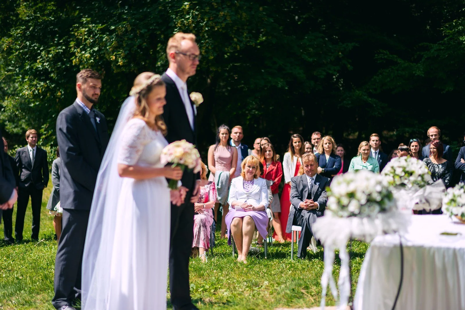 Muž v šedé vestě a motýlku stojí ve dveřích, zachycený přes rozostřené popředí.