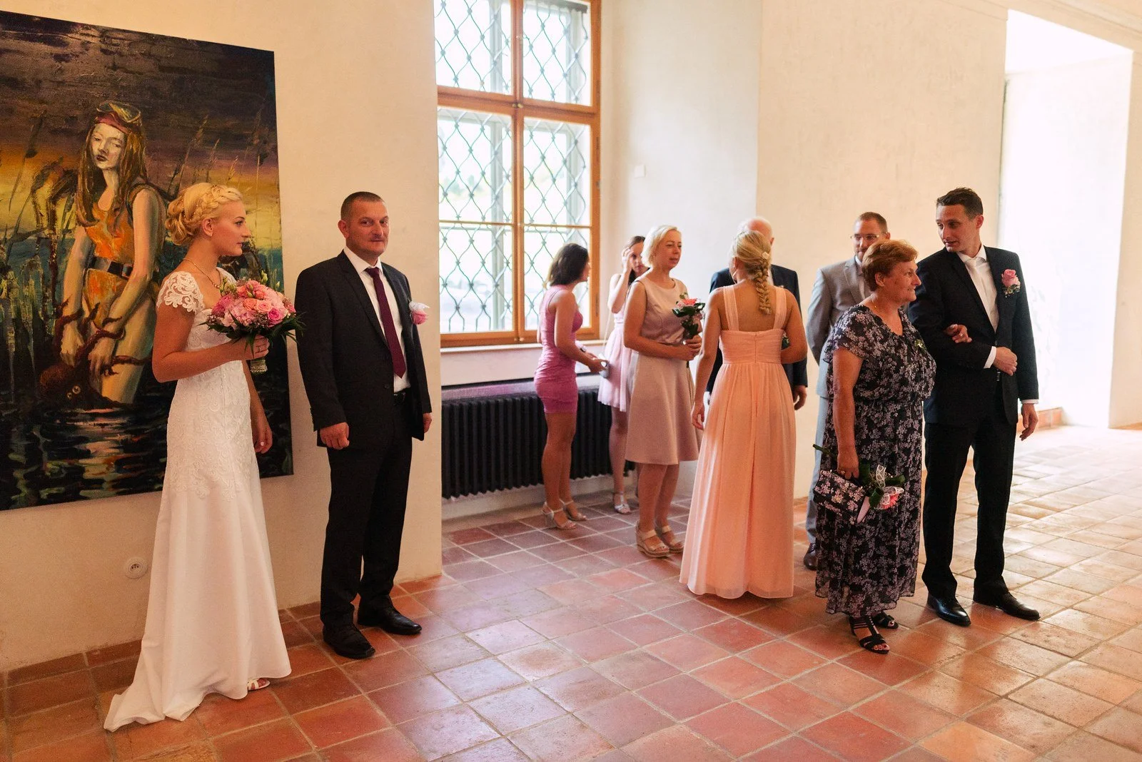 Dvojice ve slavnostním oblečení stojí před hosty v obřadní síni.