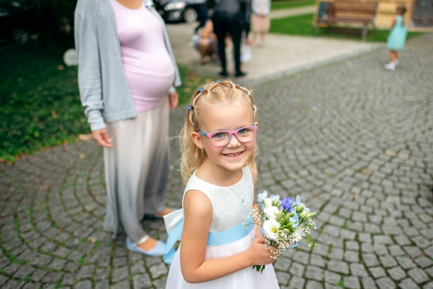 Dívka s brýlemi drží drobnou kytici na nádvoří.