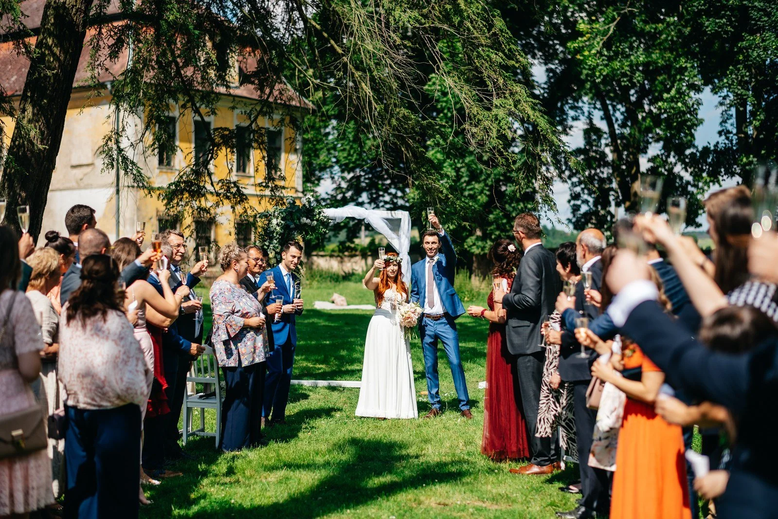 Hosté lemují cestu a zvedají ruce nad procházející dvojicí.