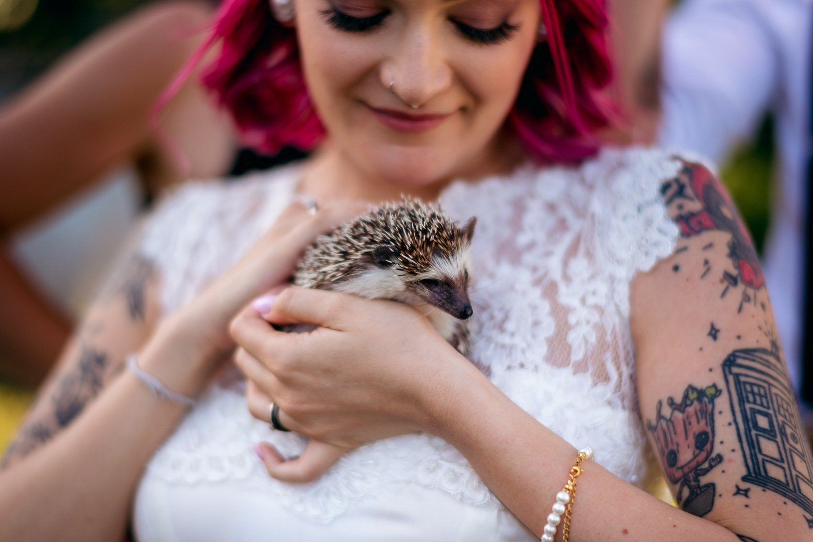 Potetovaná žena s růžovými vlasy drží v náručí usměvavé dítě.