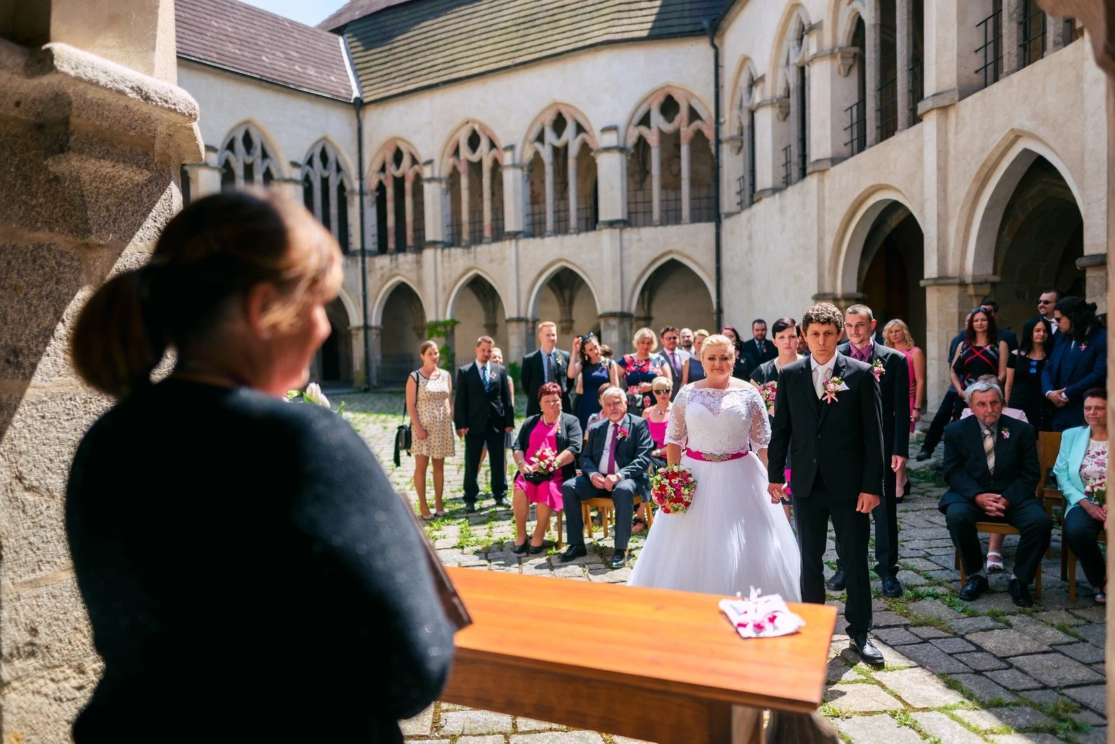 Široký pohled přes rameno řečníka ukazuje obřad i zaplněné nádvoří.