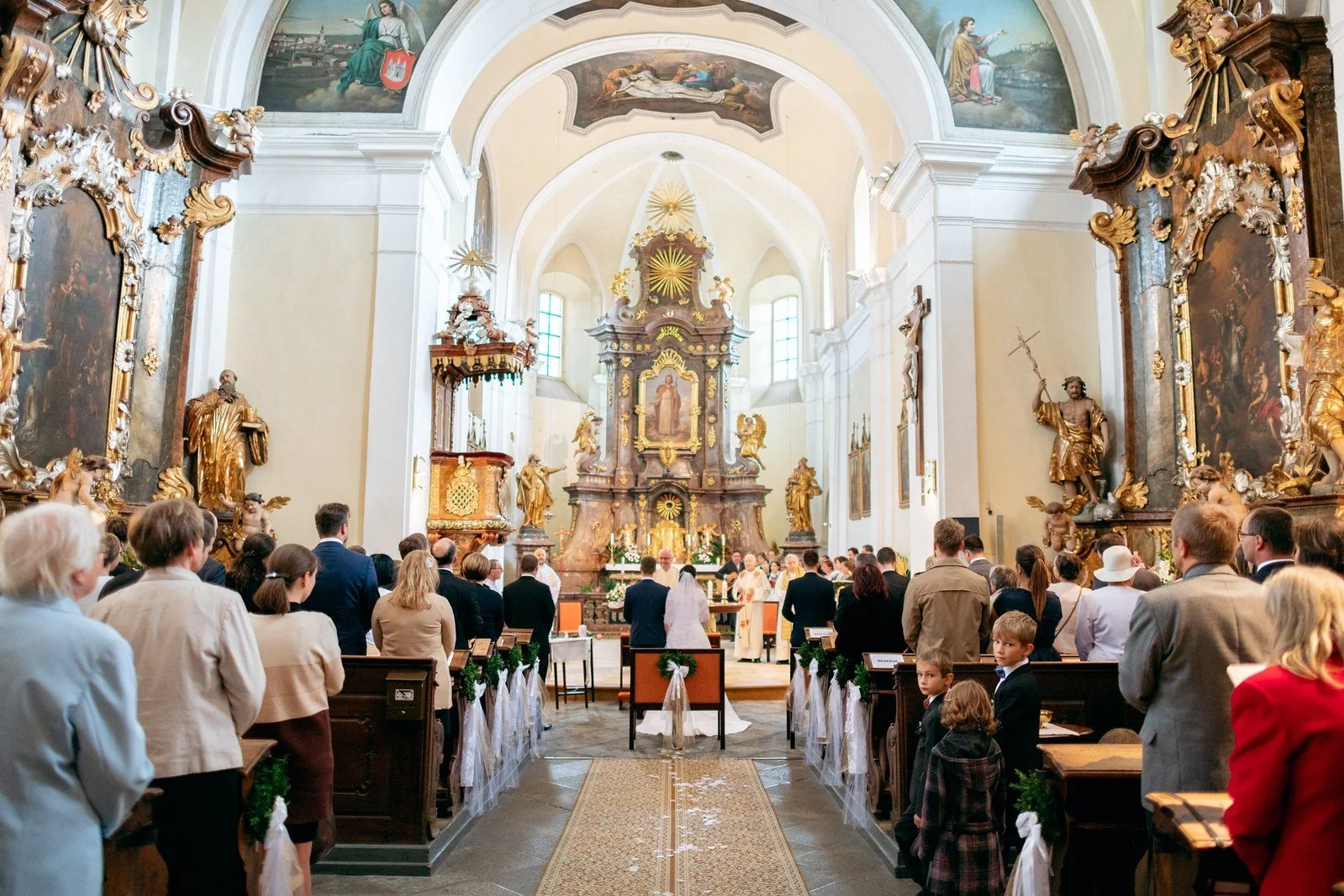 Široký pohled zezadu ukazuje zaplněnou kostelní loď, vysoké klenby a zdobený oltář.